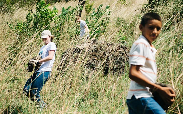 several people carry large rocks on grassy hill