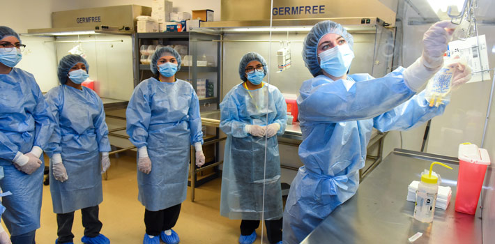 Prospective student practices a stethoscope on a dummy laying in a bed