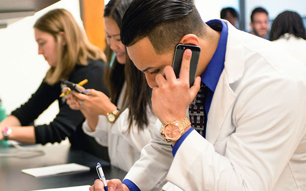 Pharmacy students work busily talking on phones, writing and typing