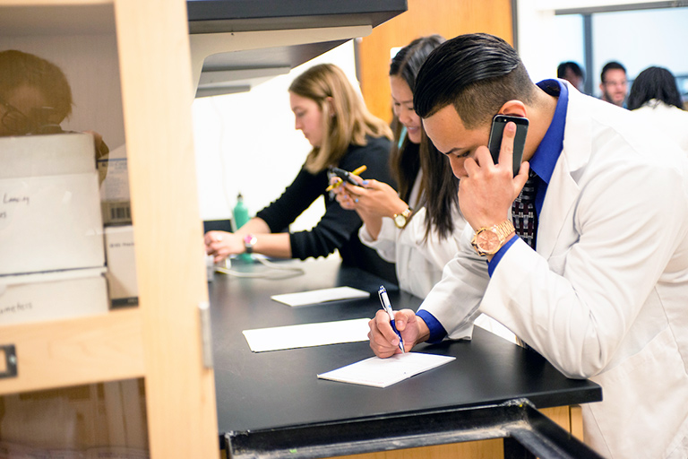 students work busily, taking calls and writing, in the the pharmacy lab on the Regis University campus