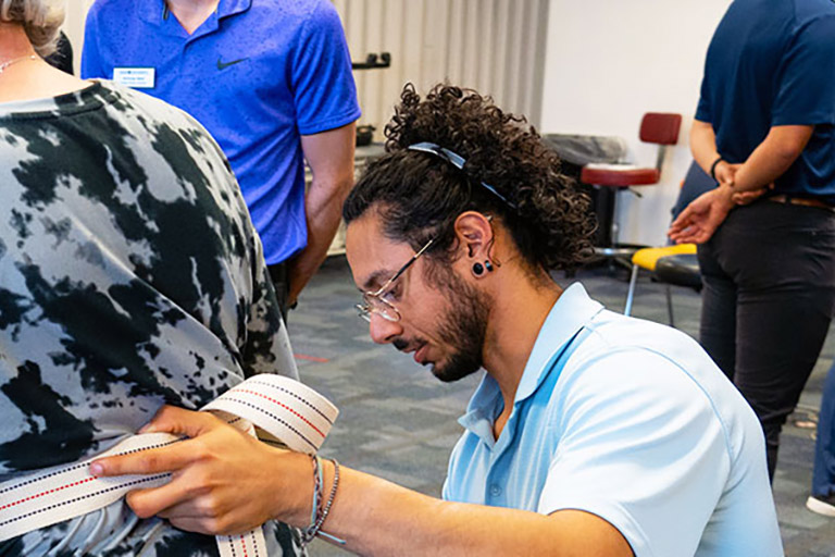a student in the Regis physical therapy program steadies a patient as she performs a walking exercise in the simulation lab