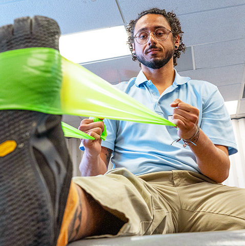 a Regis physical therapy student demonstrates a stretch using a resistance band in a classroom on the Denver, Colorado campus