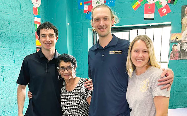Regis DPT students and faculty smile with their arms around community members at a community clinic during a service learning trip