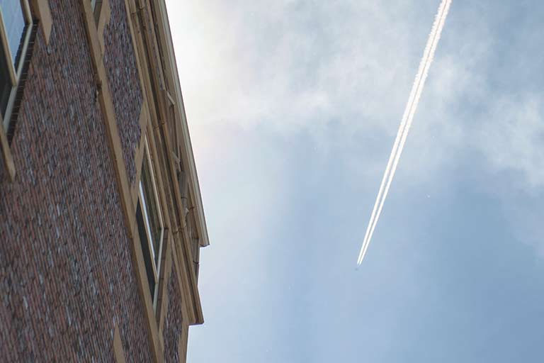Plane leaves contrails across sky beside brick building