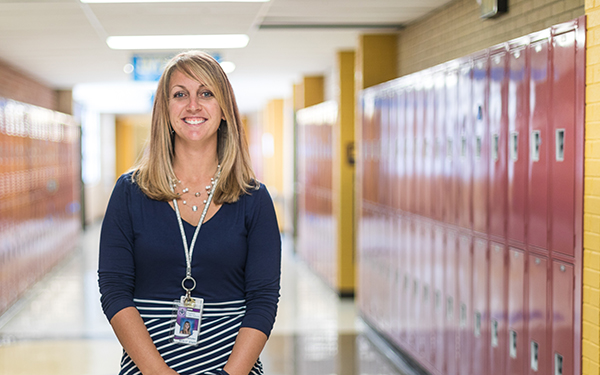 teacher stands smiling in front of lockers