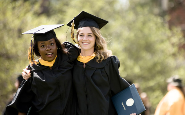 two graduates walk, hold diploma