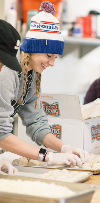 Regis University students and volunteers preparing food together in a kitchen.
