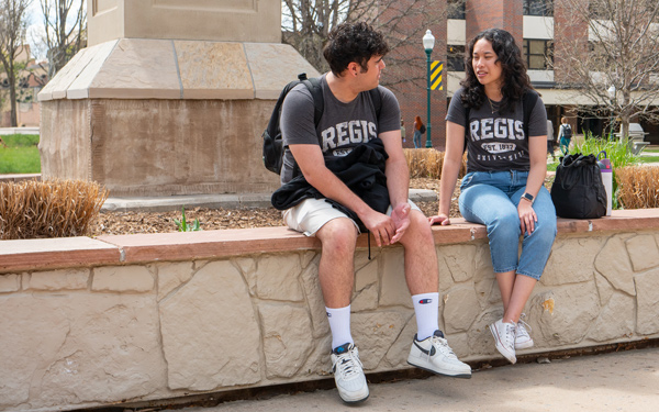 Two students chatting and sitting outside by a statue