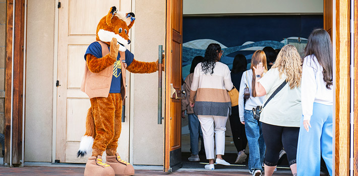 Regi the Mascot holds the door and welcomes students to the St. John Francis Regis Chapel on the Denver campus