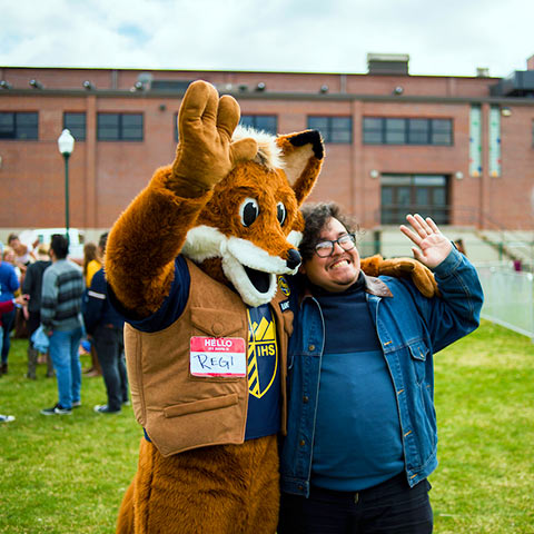 A young person poses for a photo with Regis the Fox on the Northwest Denver campus