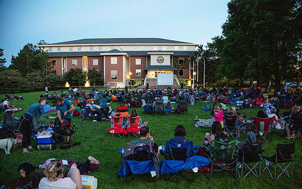 People sit on the grass of the Quad while a movie is being played on an inflatable screen in front of them