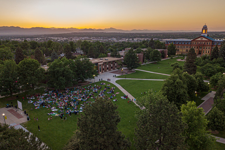 Aerial view of a Regis Northwest Denver campus at sunset with a crowd on the green lawn watching an outdoor movie
