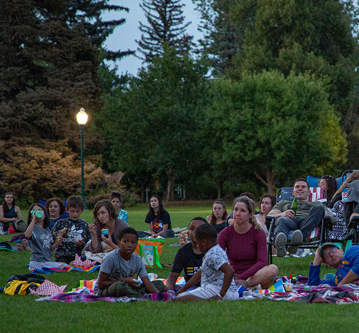 families sit on the grass on blankets and camp chairs