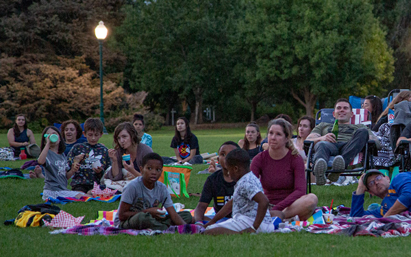 families sit on the grass on blankets and camp chairs