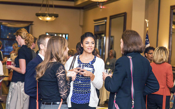a large group of prospective students, faculty, staff and alumni talk and enjoy food and wine at an evening event