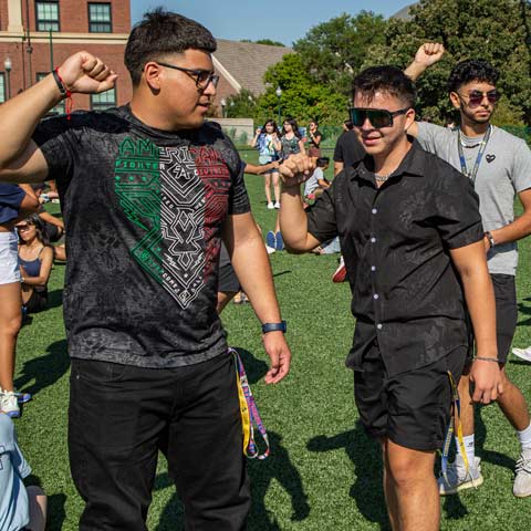Students raising their arms and interacting during an outdoor campus activity.