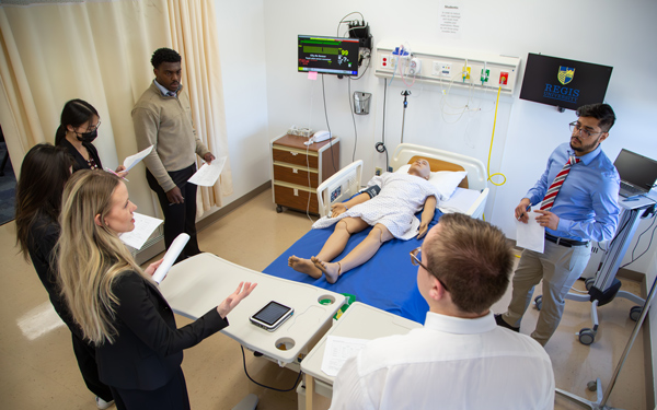 A group of medical professionals gathers around a hospital bed with a mannequin for training