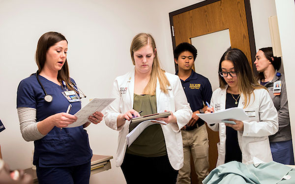 students wearing white coats, scrubs and business casual collaborate on a project on the Interprofessional Thornton campus