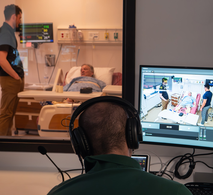 Student monitoring a patient simulation on a screen from an observation room