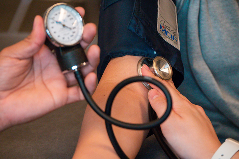 Close-up of student using stethoscope and blood pressure cuff on another student for a blood pressure reading