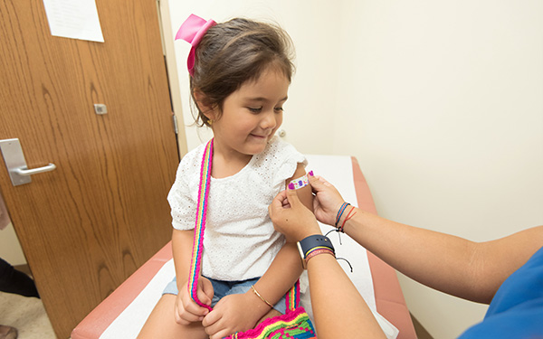 person wearing scrubs applies a bandage to smiling child's arm