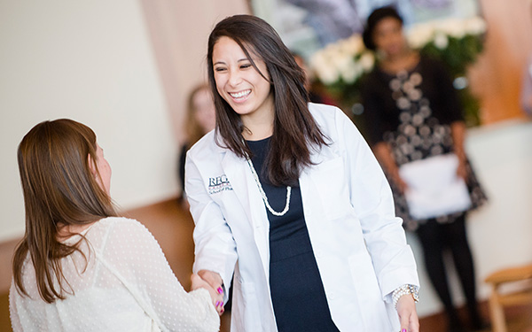 Graduate receiving her white coat and shaking a professors hand