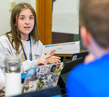 an RMCCDC participant smiles while networking with a fellow competitor in the Mountain View Room in Claver Hall on the Regis campus