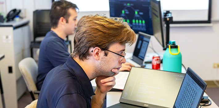 two RMCCDC competitors work intently on multiple laptops and screens