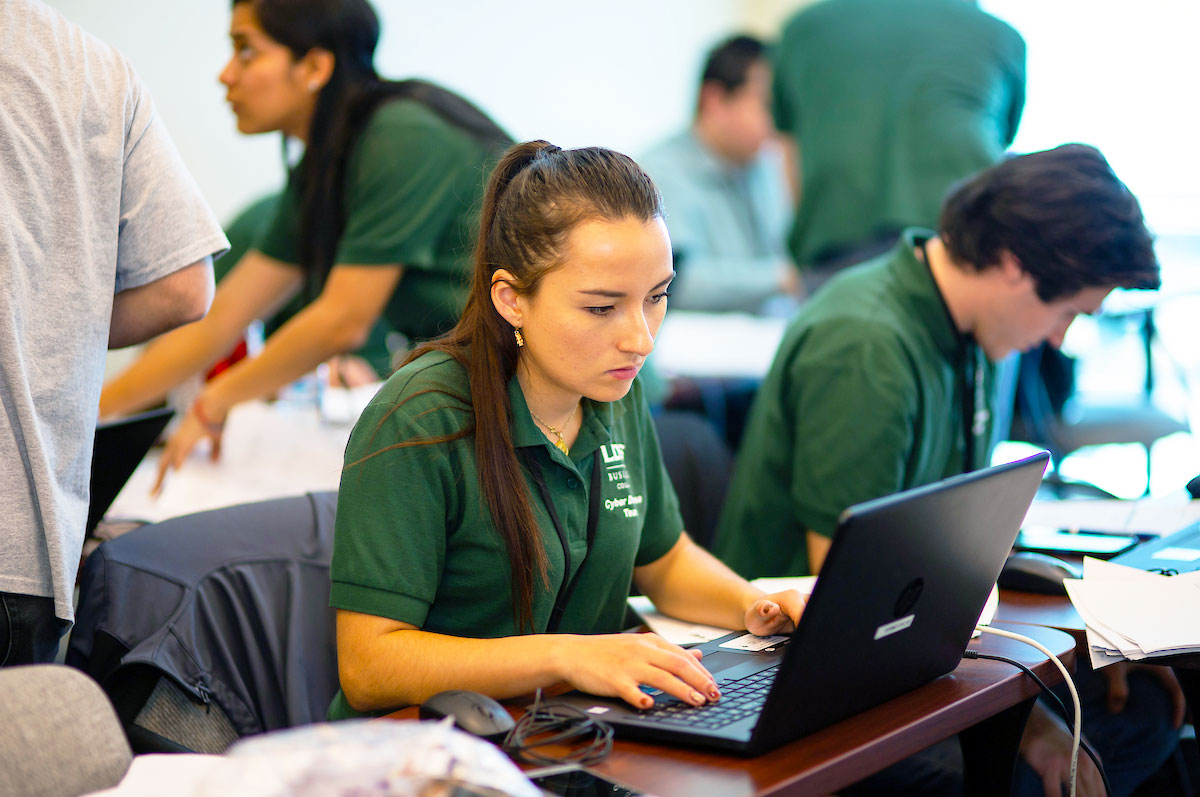 students wearing matching green polos look intently at laptops and chat intensely while competing as the green team at RMCCDC