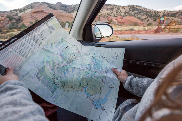 Person sitting in a car looking at a park map with red rock formations visible outside the window