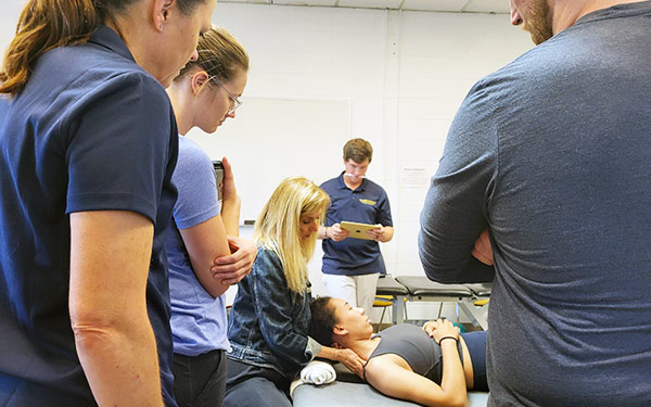 a Orthopaedic Physical Therapy Residency faculty member demonstrates a technique on a student laying on a table while the rest of the class observes in a classroom on the Denver, Colorado campus