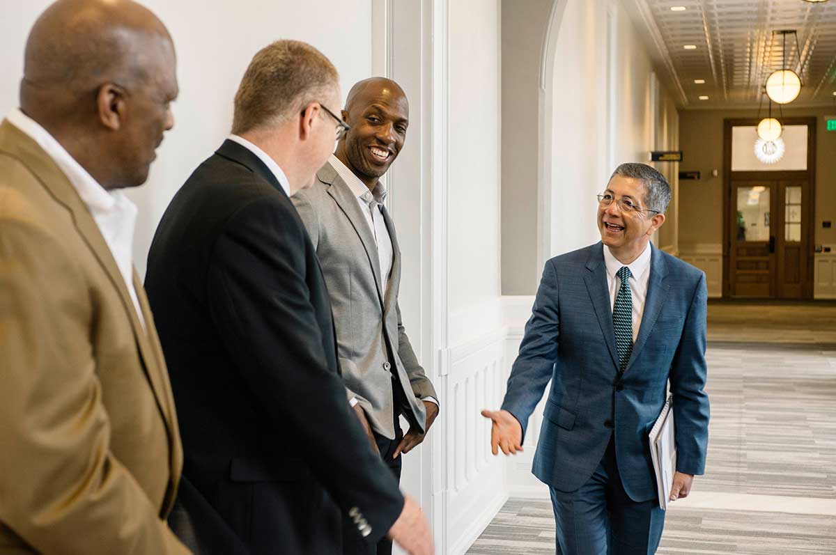Aceves shakes hands with Chauncy Billups, Lonnie Porter and another man in the hallway of Main Hall