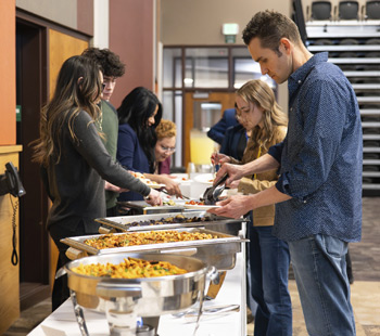 People on the right dishing up food onto their plates while those on the left are dishing food from the same table.