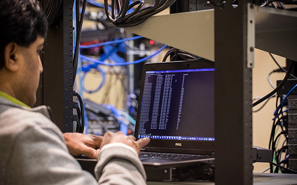 man in server room types on computer displaying code