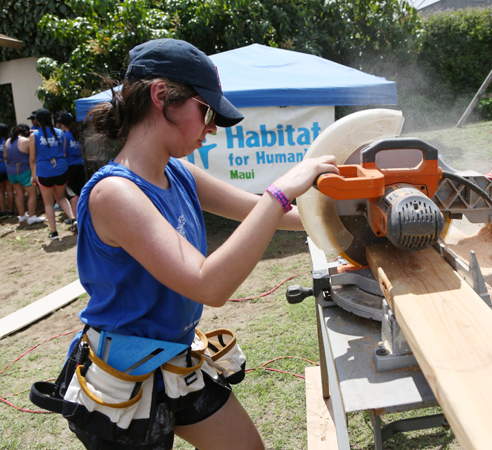 Regis University student volunteering on a Habitat for Humanity build, cutting lumber with a power saw