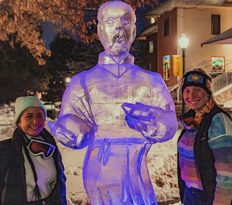 Students enjoying a winter campus event and posing with an illuminated ice sculpture.