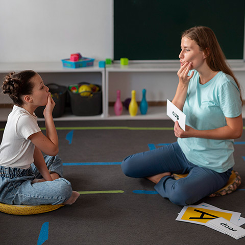 Speech language pathologist showing a child how to form sounds using flashcards and demonstration