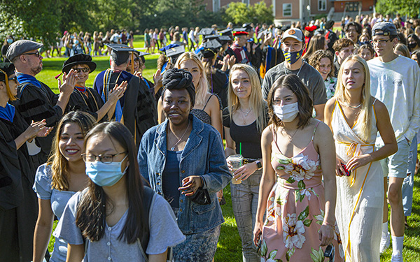 a large crowd of students winds around the Quad flanked by applauding faculty in regalia at Spring Convocation