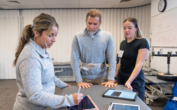 Two Regis students collect data on tablets with physical therapy patient