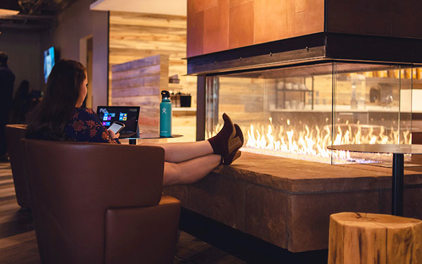 woman sits working on her phone and laptop with her feet up on the fireplace in the student center