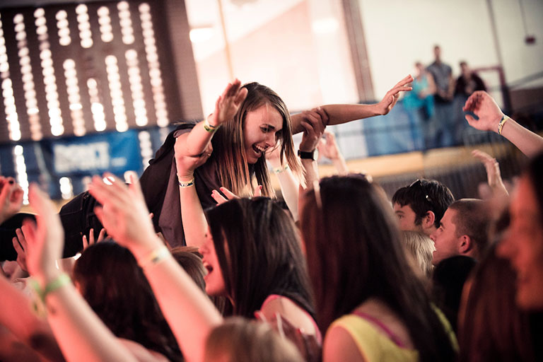 A young woman crowdsurfs while concert goers observe the stage