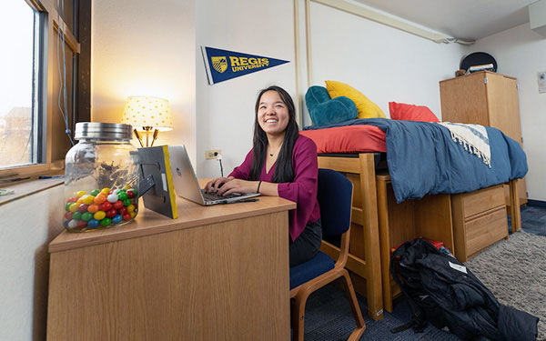 a student works on her laptop on the desk in her dorm room