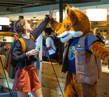 Regis University student high-fiving Regi the Ranger mascot inside a campus café