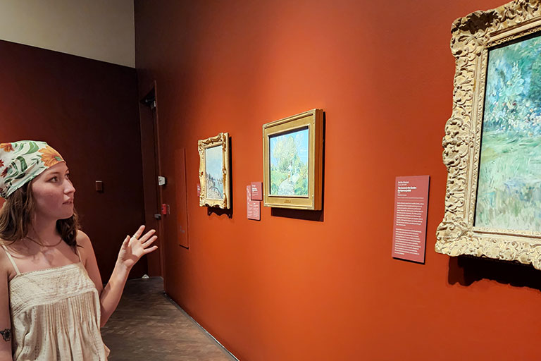 woman gestures at a painting on the wall in a gallery