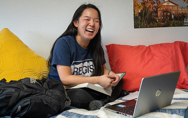 Student smiles and sits on the bed in her dorm room