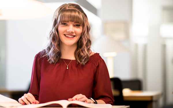 A student smiles while studying in a well-lit library.