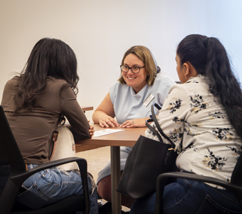A student and parent sit at a table facing towards a Regis staff member who is smiling back at them