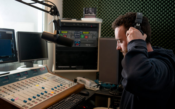 Regis University student working in a campus radio studio with audio equipment.