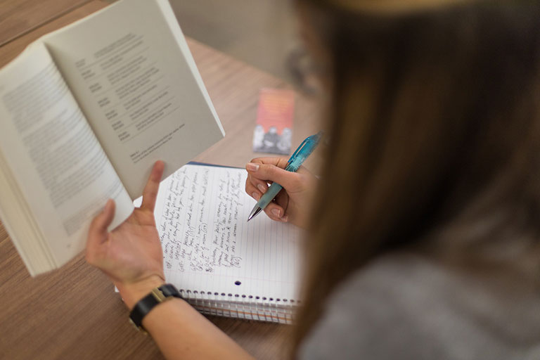 A student takes notes while reading from a book