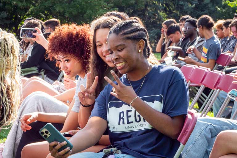Student smiling and taking a selfie with friends while seated at an outdoor event.